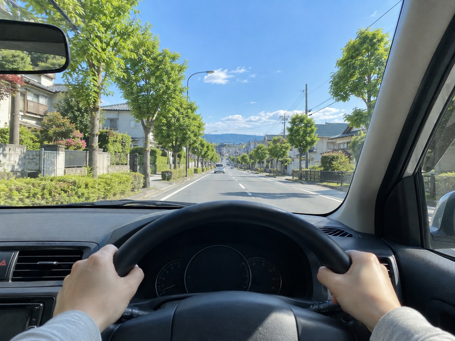 ハンドル越しに青空と緑のある道を望む、晴れた日のドライブのイメージ